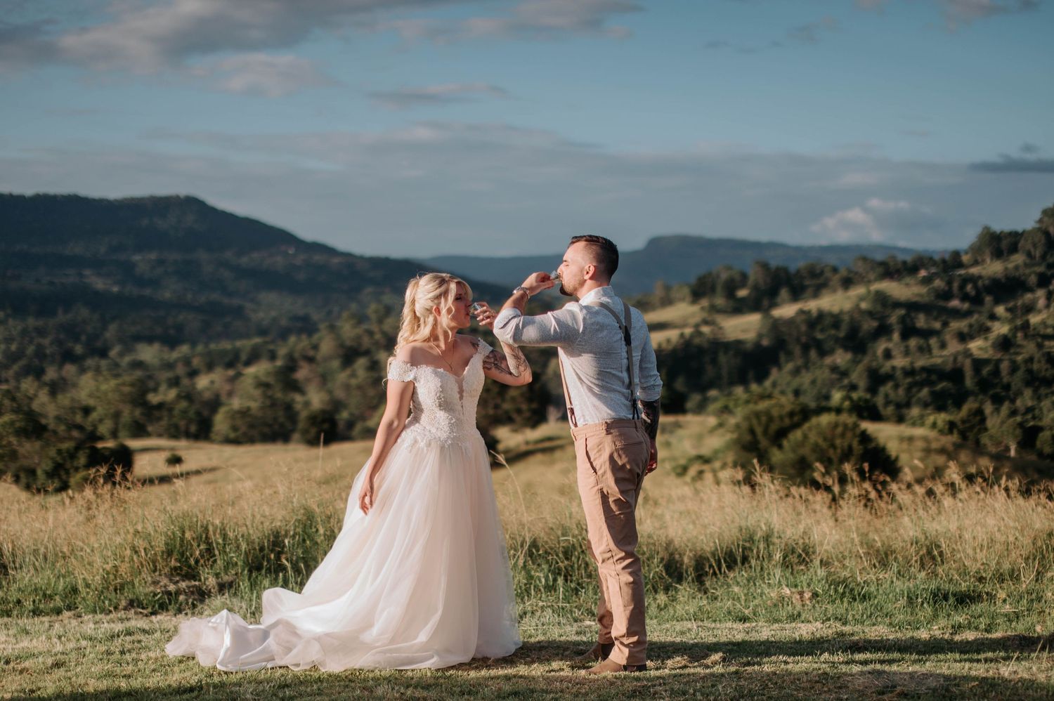 Wedding couple standing on hilltop overlooking mountain landscape.