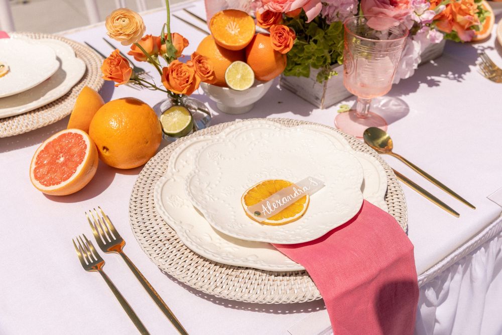 Elegant citrus-themed wedding table setting with oranges, grapefruit, roses, and gold cutlery.