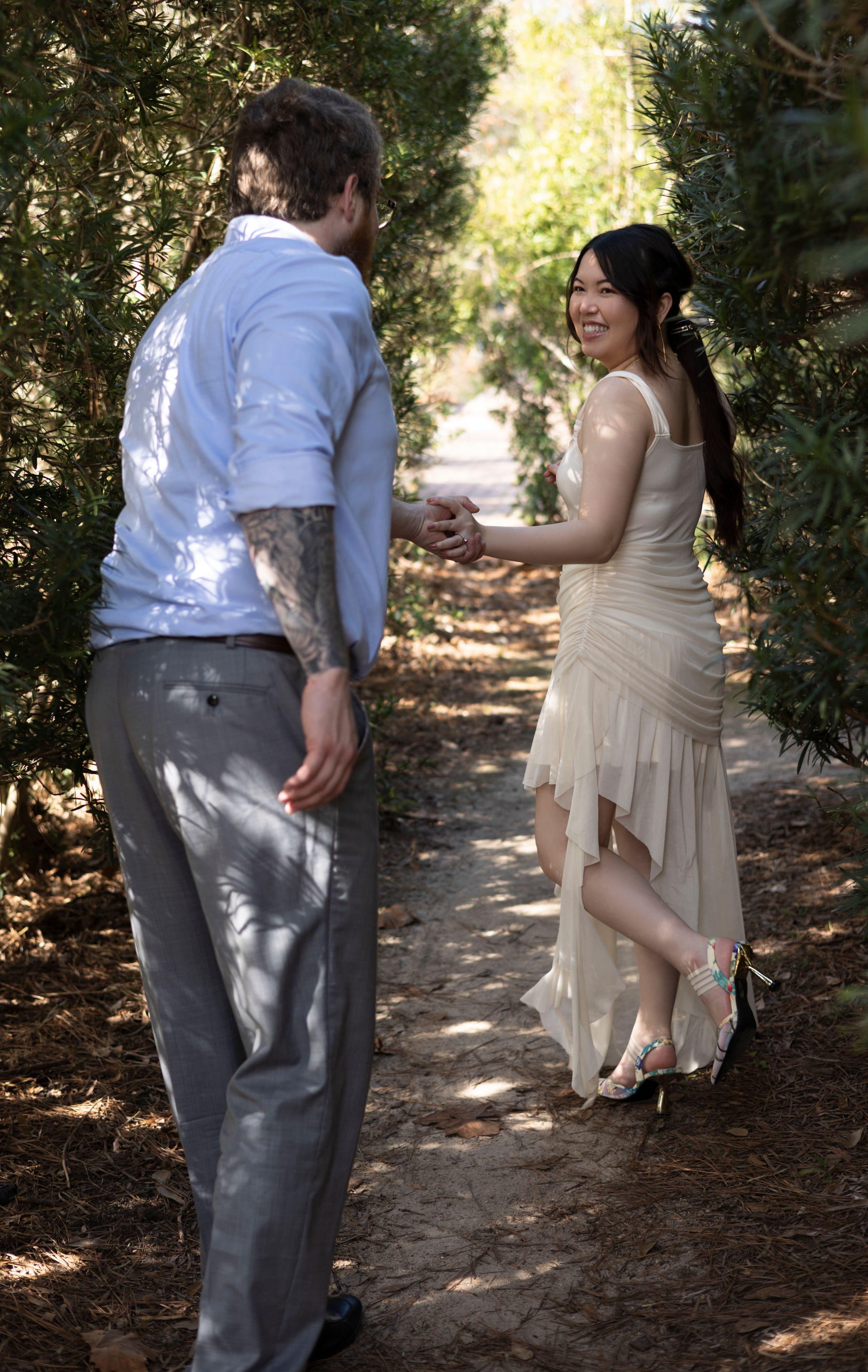 A couple shares a joyful moment on a sunlit garden path during their wedding photo session.