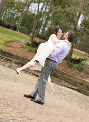 Couple shares a romantic moment on brick paving as groom lifts bride in white dress during sunny outdoor photo session.