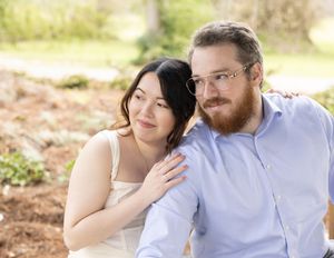 A couple sits together outdoors in a natural setting with soft sunlight and bokeh background.