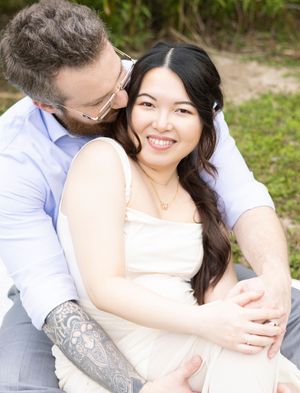 A couple sits together outdoors sharing an intimate embrace while wearing white and light colored clothing.