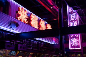 Colorful neon signs illuminate a building facade in purple and red hues creating a cyberpunk aesthetic at night.