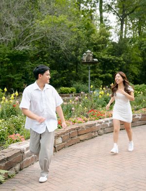 Two people in casual attire enjoying a playful moment together on a brick path in a lush garden setting.