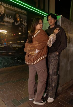 Two people pose closely together at night against a wall with neon green lighting in an urban setting.
