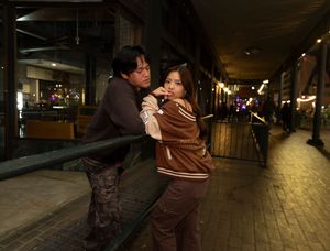 People in brown jackets lean against railing on illuminated city street at night.