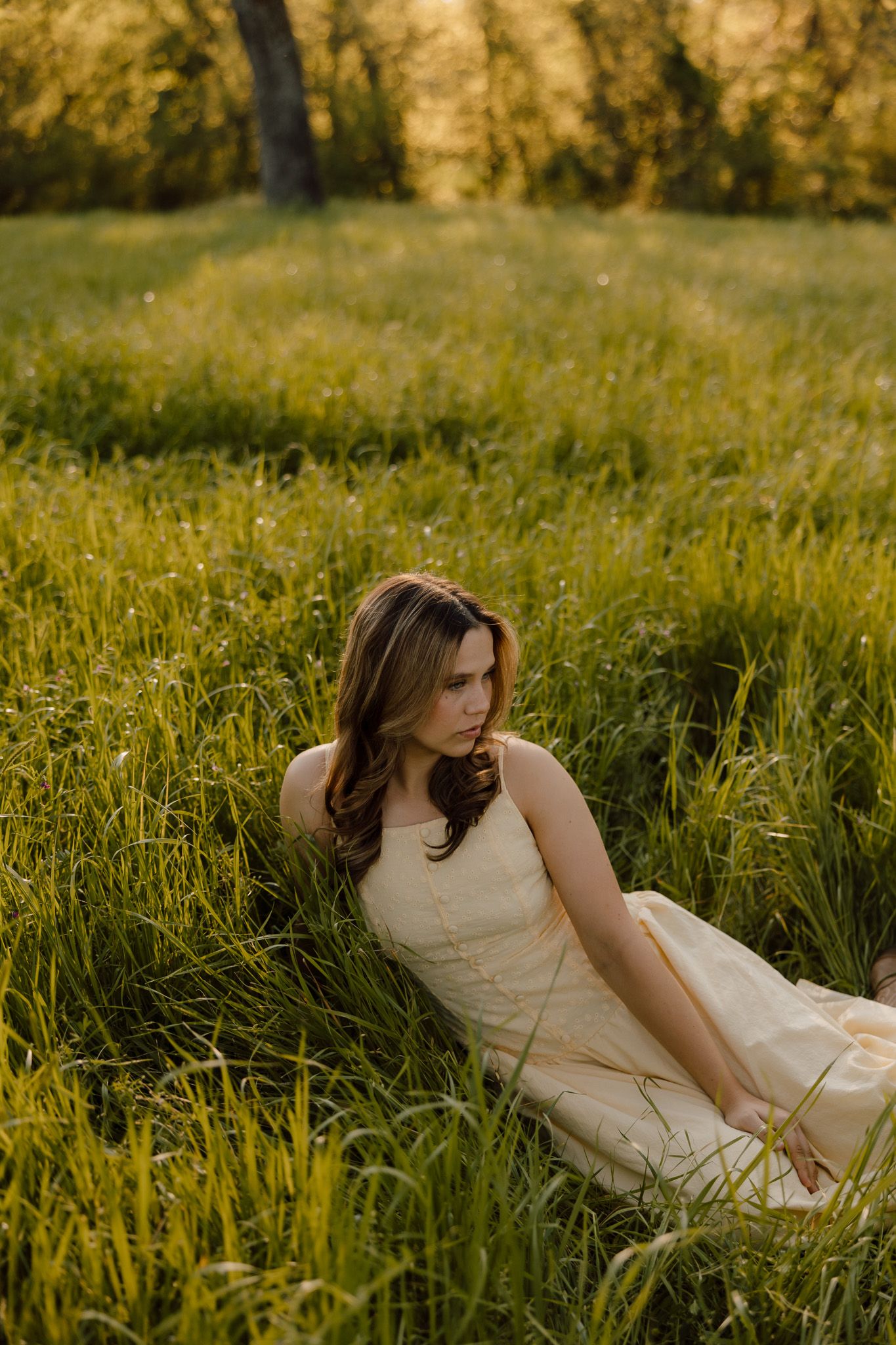 Woman in white dress twirls in golden field at sunset with mountains in background.
