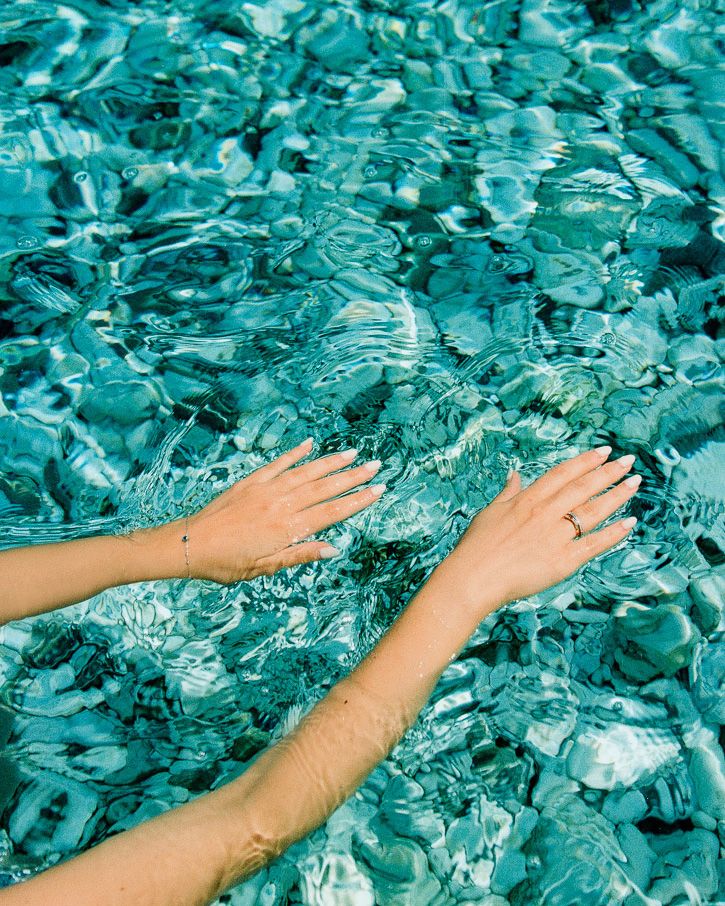 Two hands reaching through shimmering blue water, catching ripples and light.