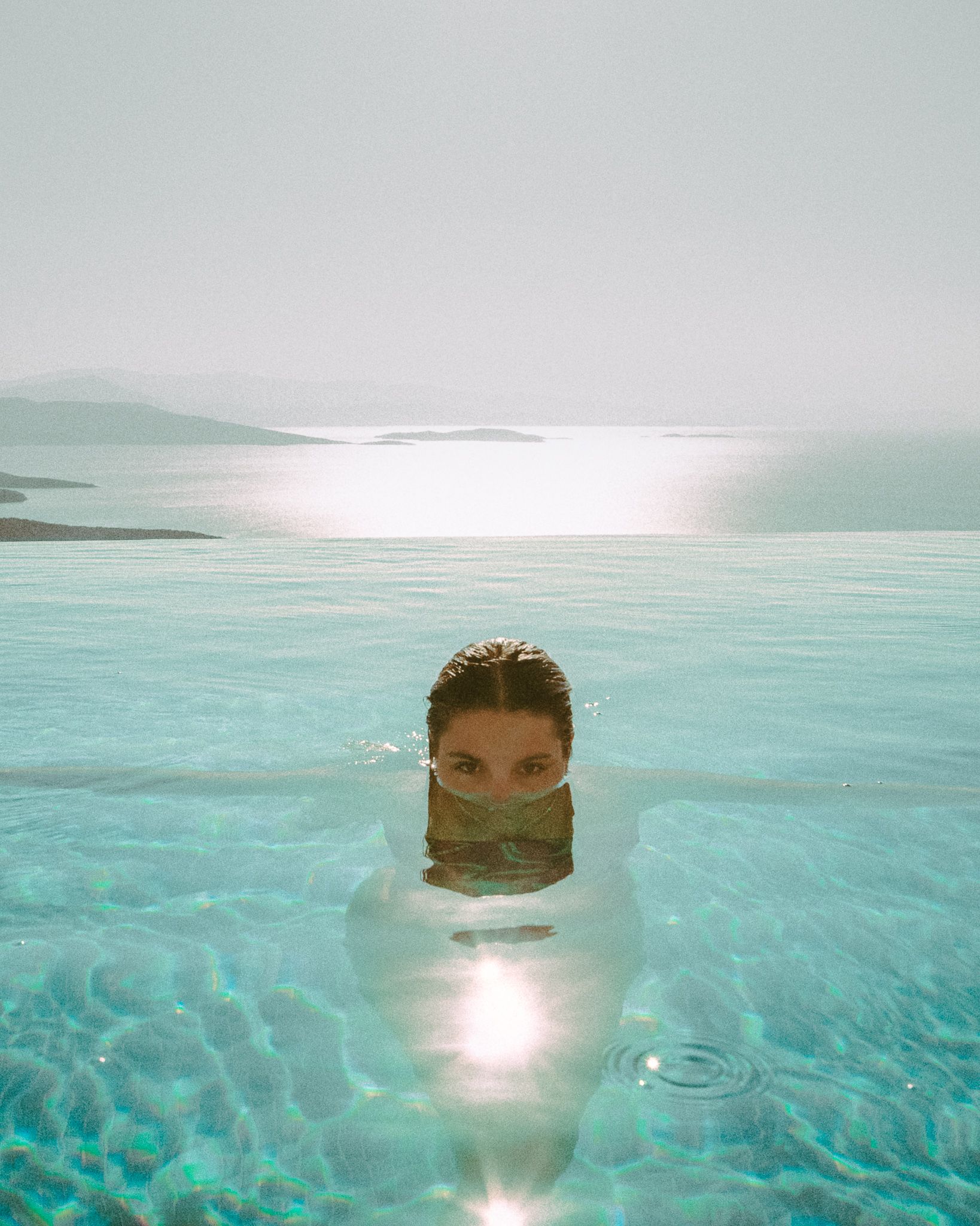 Woman partially submerged in still water, eyes above the surface, bathed in golden light.