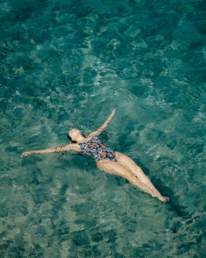 Woman floating on her back in crystal-clear water, arms spread, serene expression.