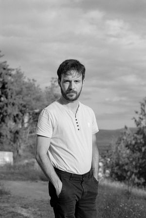 Black and white portrait of a young man outdoors, gazing calmly at the lens.