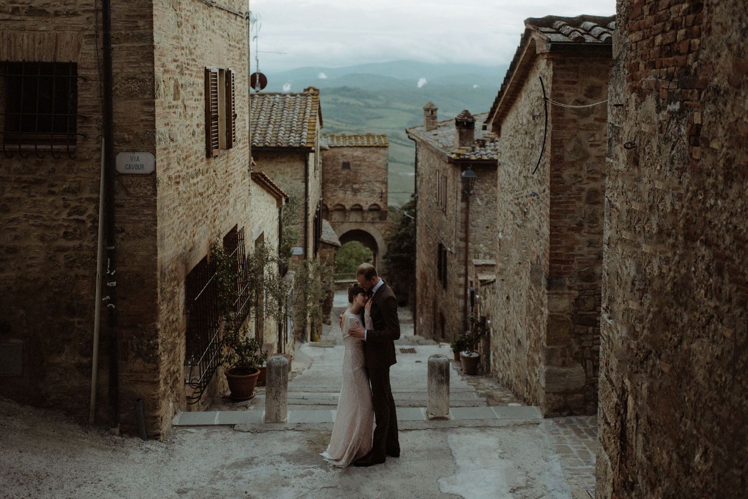 Romantic couple Jacob & Christine embraces in a narrow cobblestone street of an ancient Tuscan hill town at dusk. Photo by The Kitcheners.