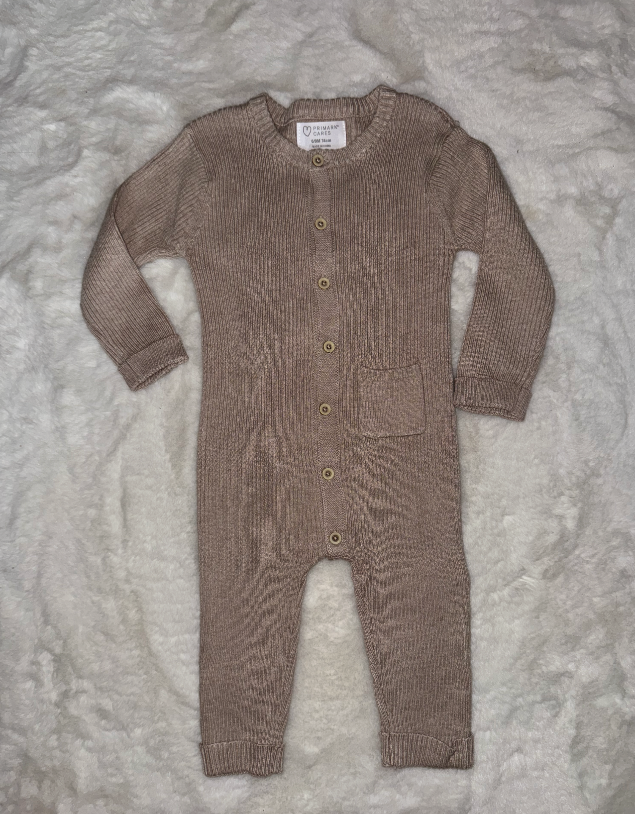 Taupe knitted baby cardigan with front pocket displayed on gray background.