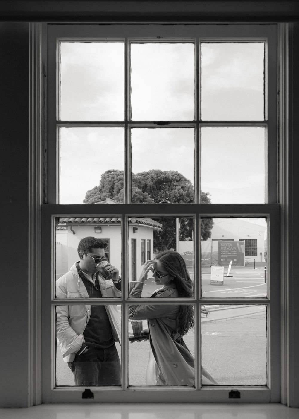 Black and white photo of two people conversing through a window pane with multiple glass sections.