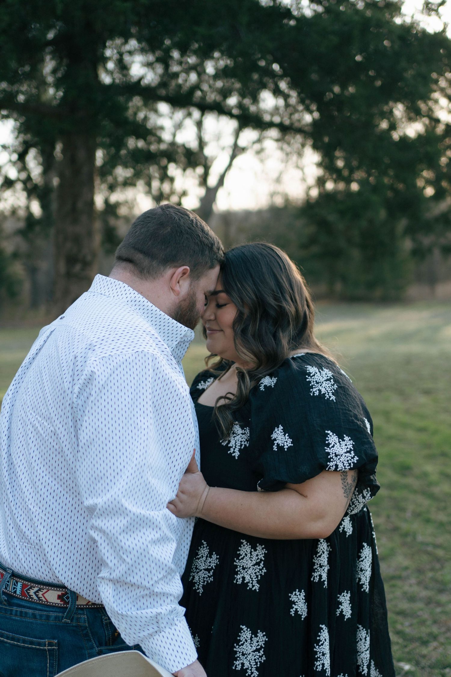 A romantic outdoor portrait shows an intimate moment between a couple wearing a white shirt and floral dress at sunset.