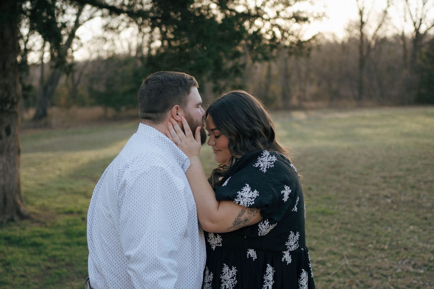 A tender moment between a couple sharing an intimate embrace in a naturalistic outdoor setting at dusk.