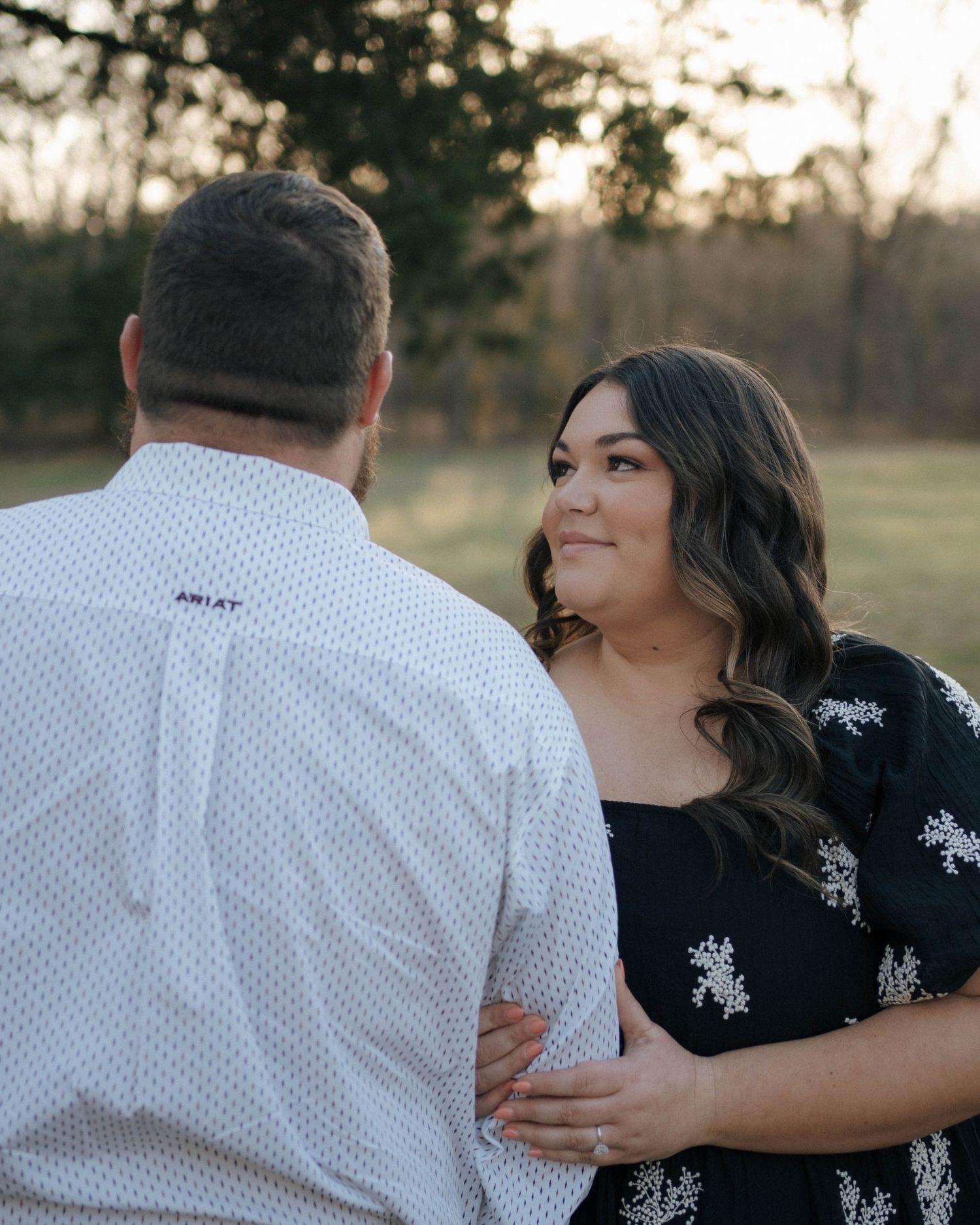 A couple embraces during a romantic sunset photoshoot, with one person wearing white and the other in a black floral dress.