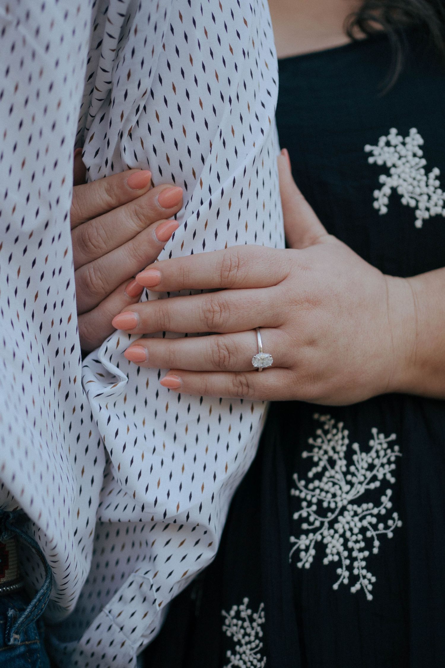 Close up of hands wearing an engagement ring against polka dot fabric and black floral dress.