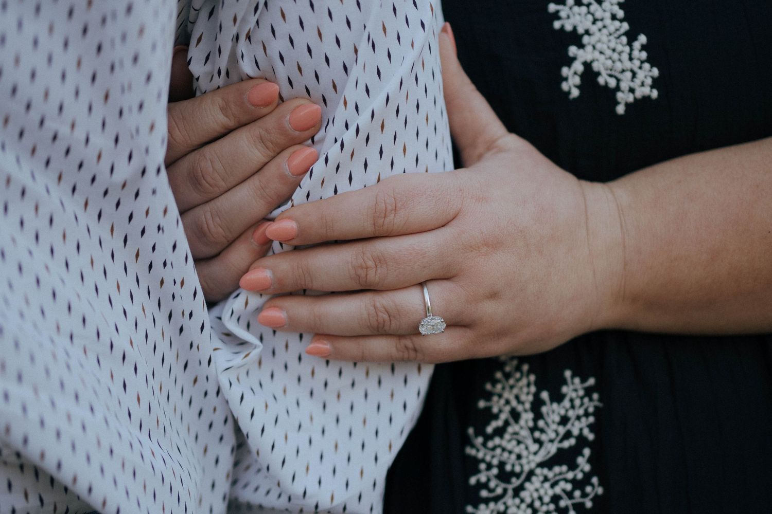 Close-up of hands with an engagement ring against a black and white patterned background.