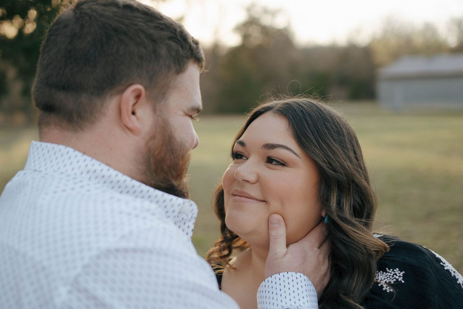 A couple share an intimate moment outdoors during a golden hour photo session, with him gently touching her face.