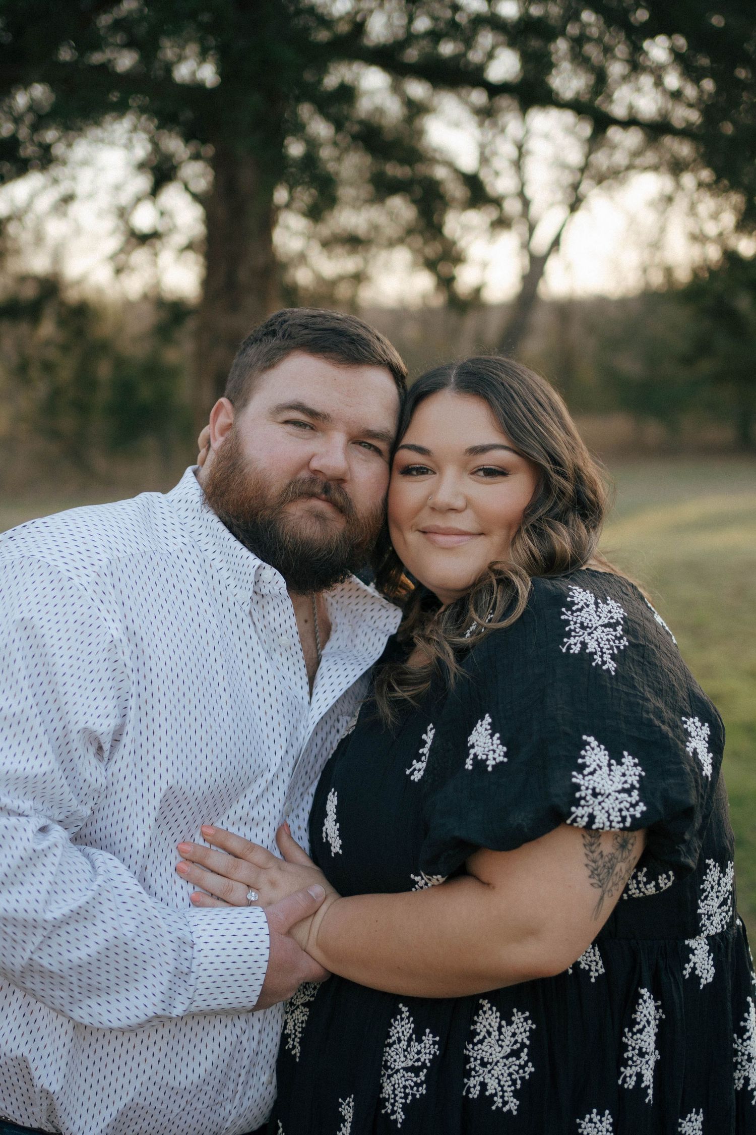 A loving couple embraces outdoors at sunset in coordinated white and black floral outfits.