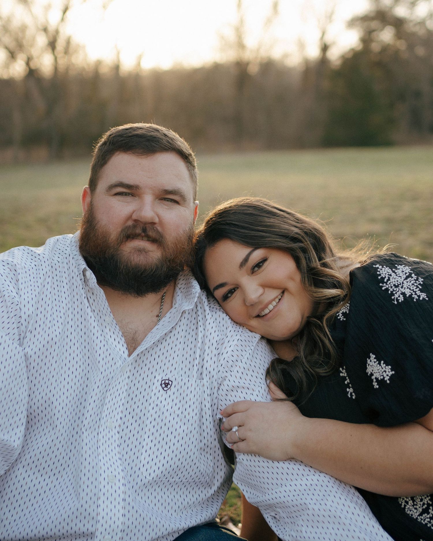 A couple shares an intimate outdoor portrait at sunset with a warm glow in a natural setting.