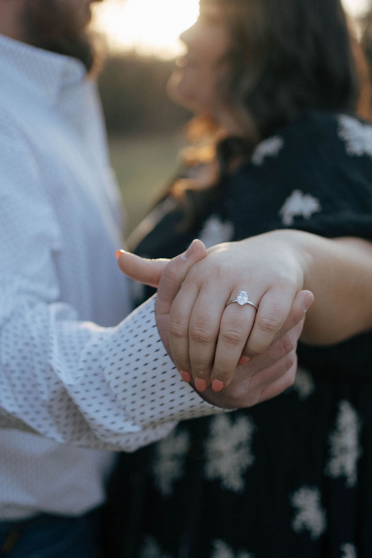 Close up of hands holding each other showing an engagement ring with sunlit background.