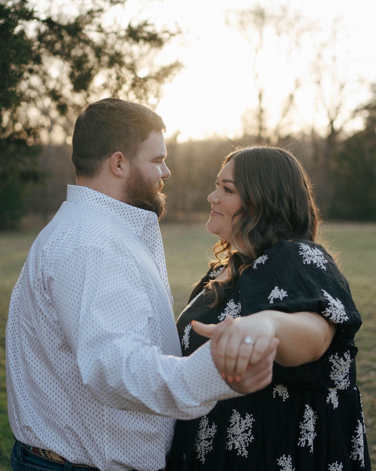A couple dances together in a romantic embrace during golden hour sunset in a field.