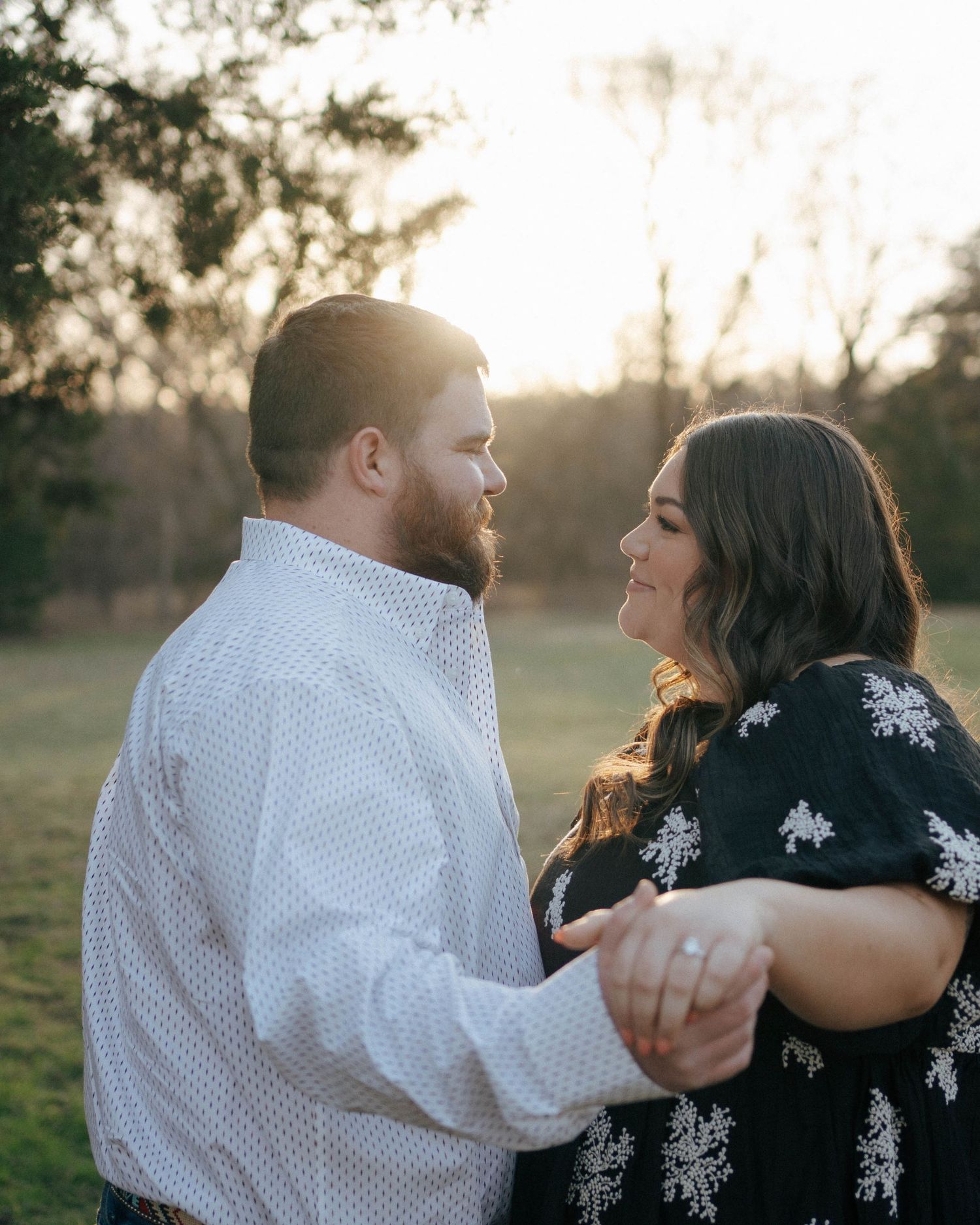 A romantic couple shares a tender moment while dancing outdoors at sunset in a field.