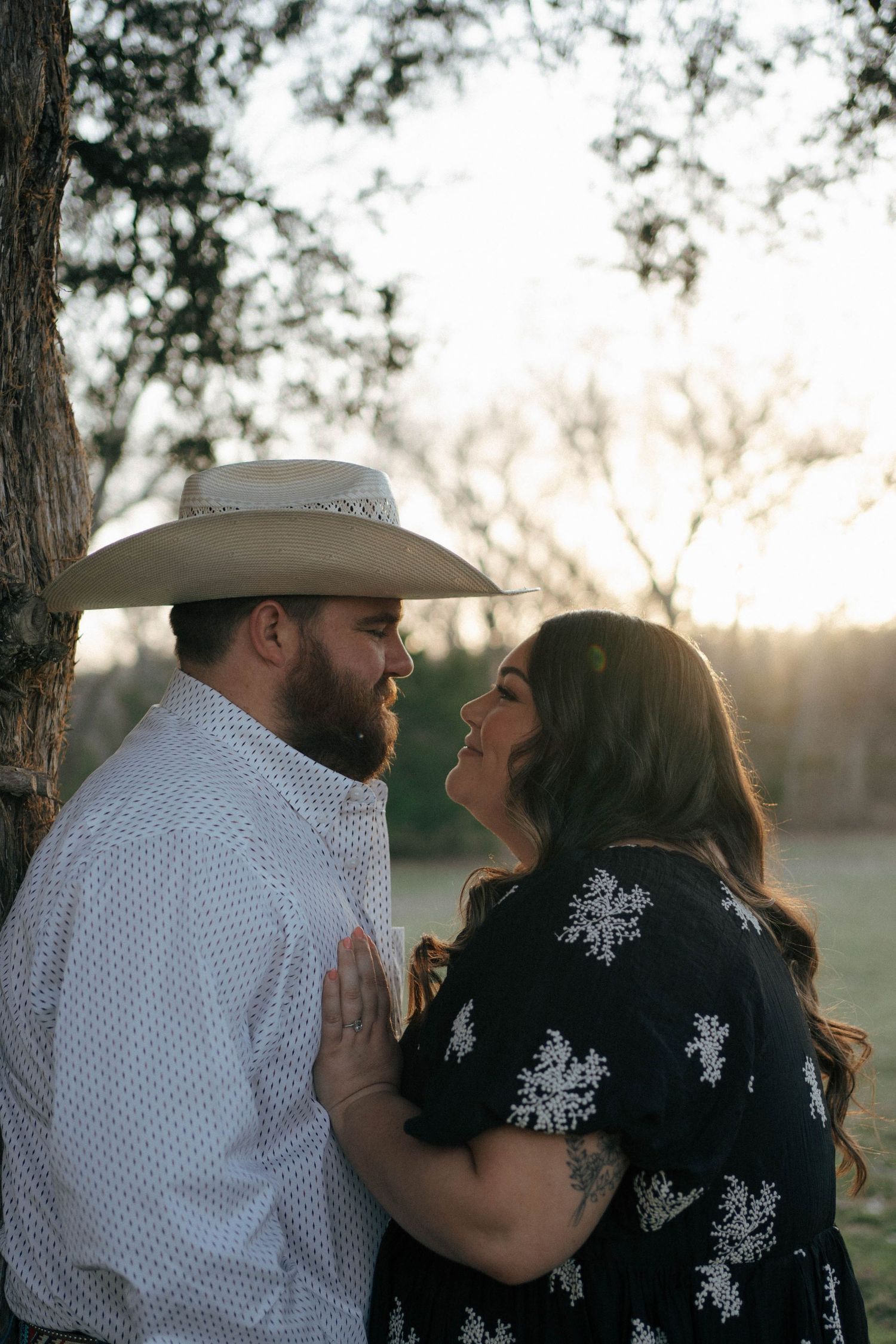A couple shares an intimate moment at sunset, with the person wearing a cowboy hat and white shirt leaning close together.