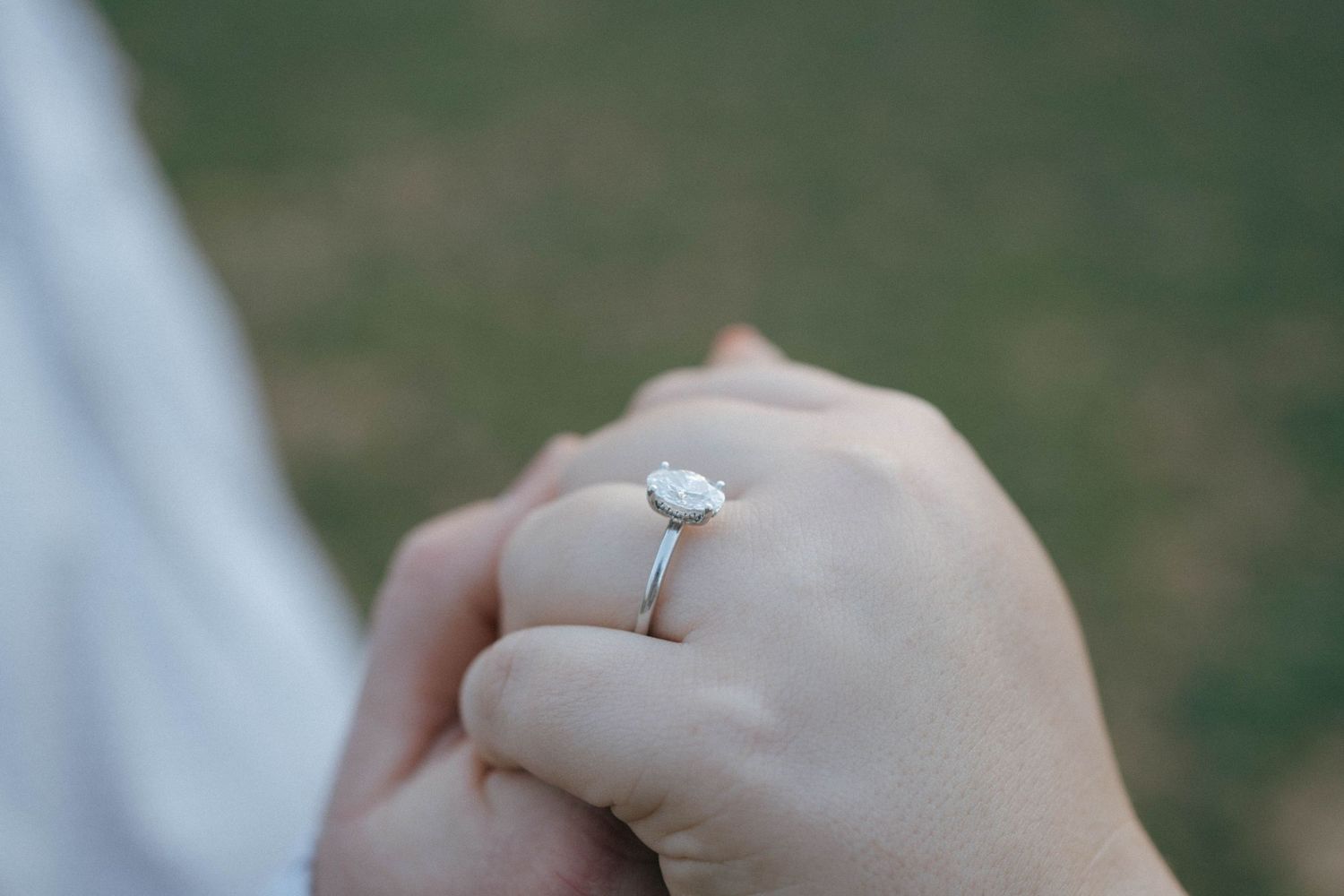 Close-up view of someone wearing a solitaire diamond engagement ring with a delicate silver band on their hand.