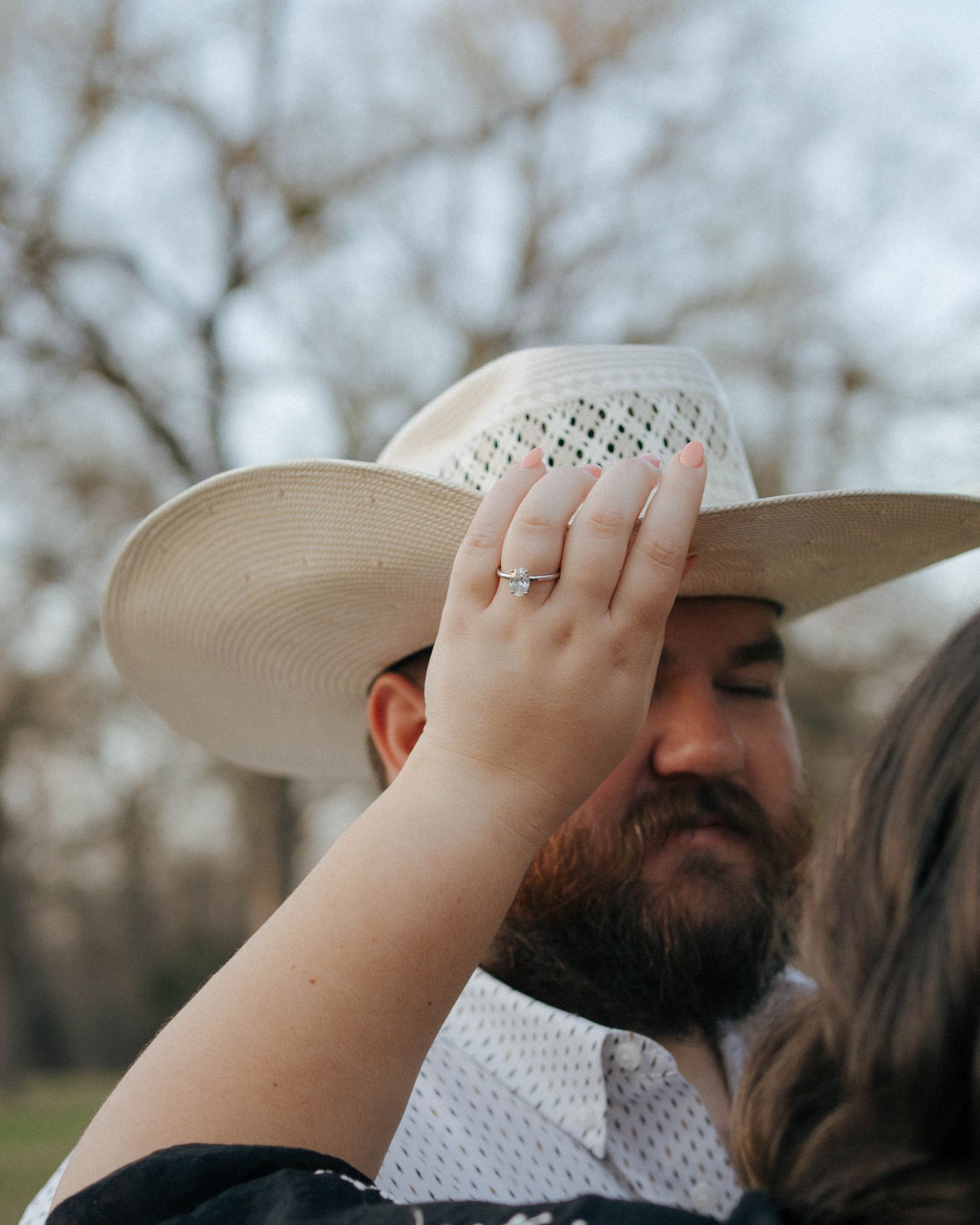 A cowboy hat perched on someone's head is gently touched by a hand with a ring.
