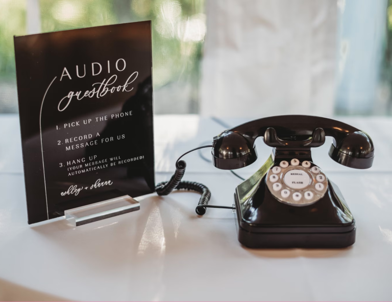 A vintage black rotary telephone next to an Audio Guestbook sign at a wedding reception.