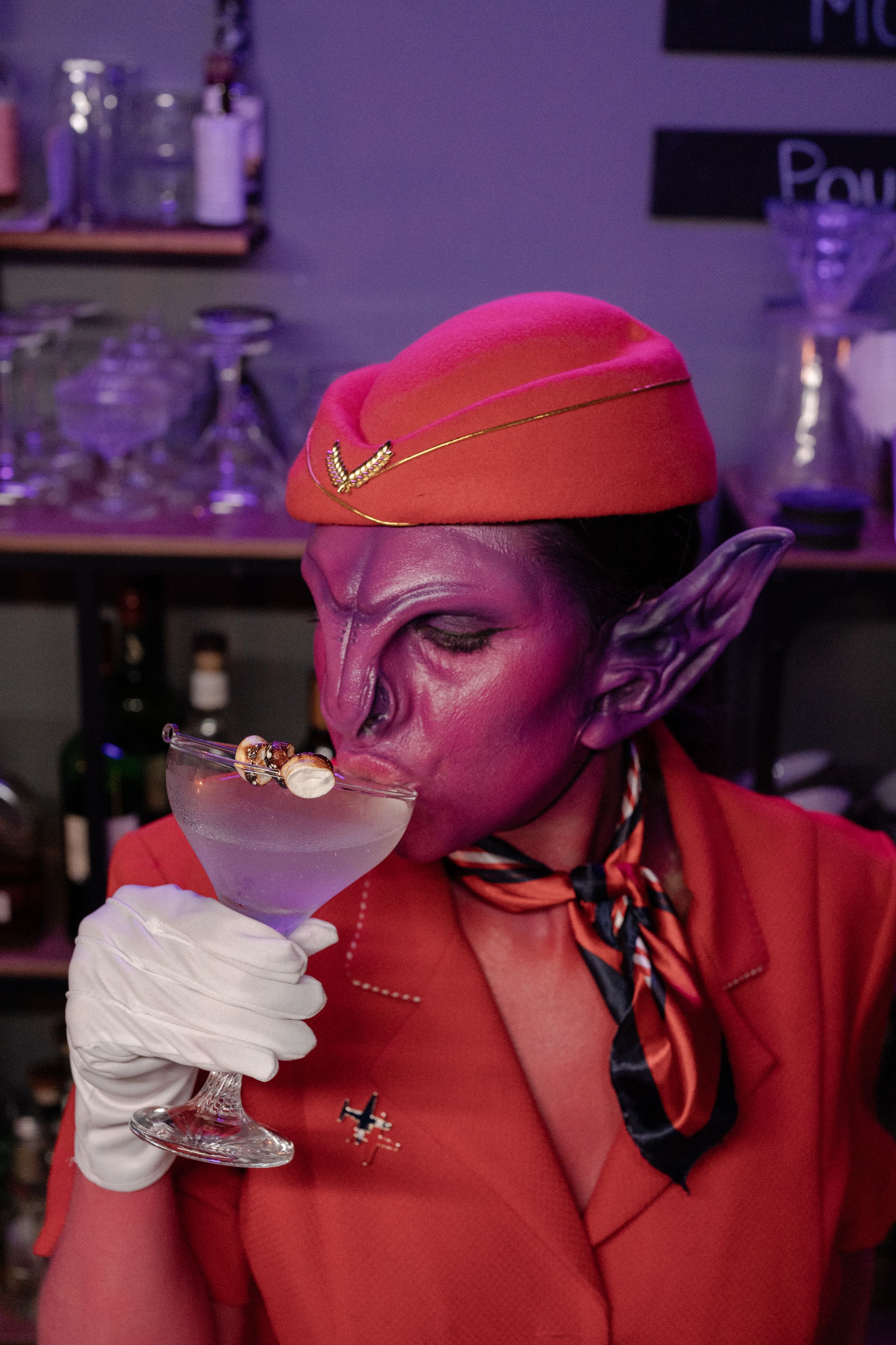 Pink alien dressed like a flight attendant making drinks.