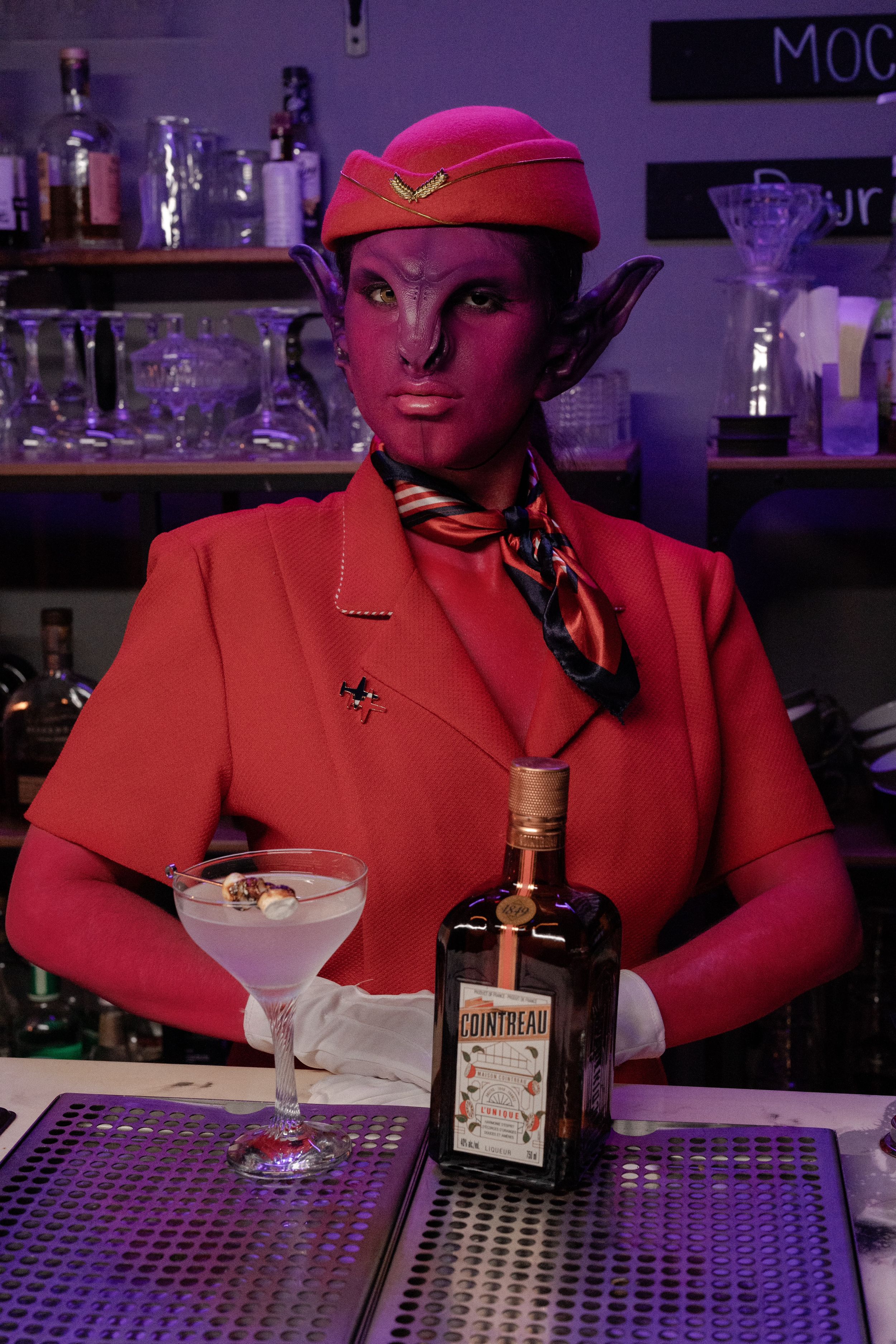 Pink alien dressed like a flight attendant making drinks.