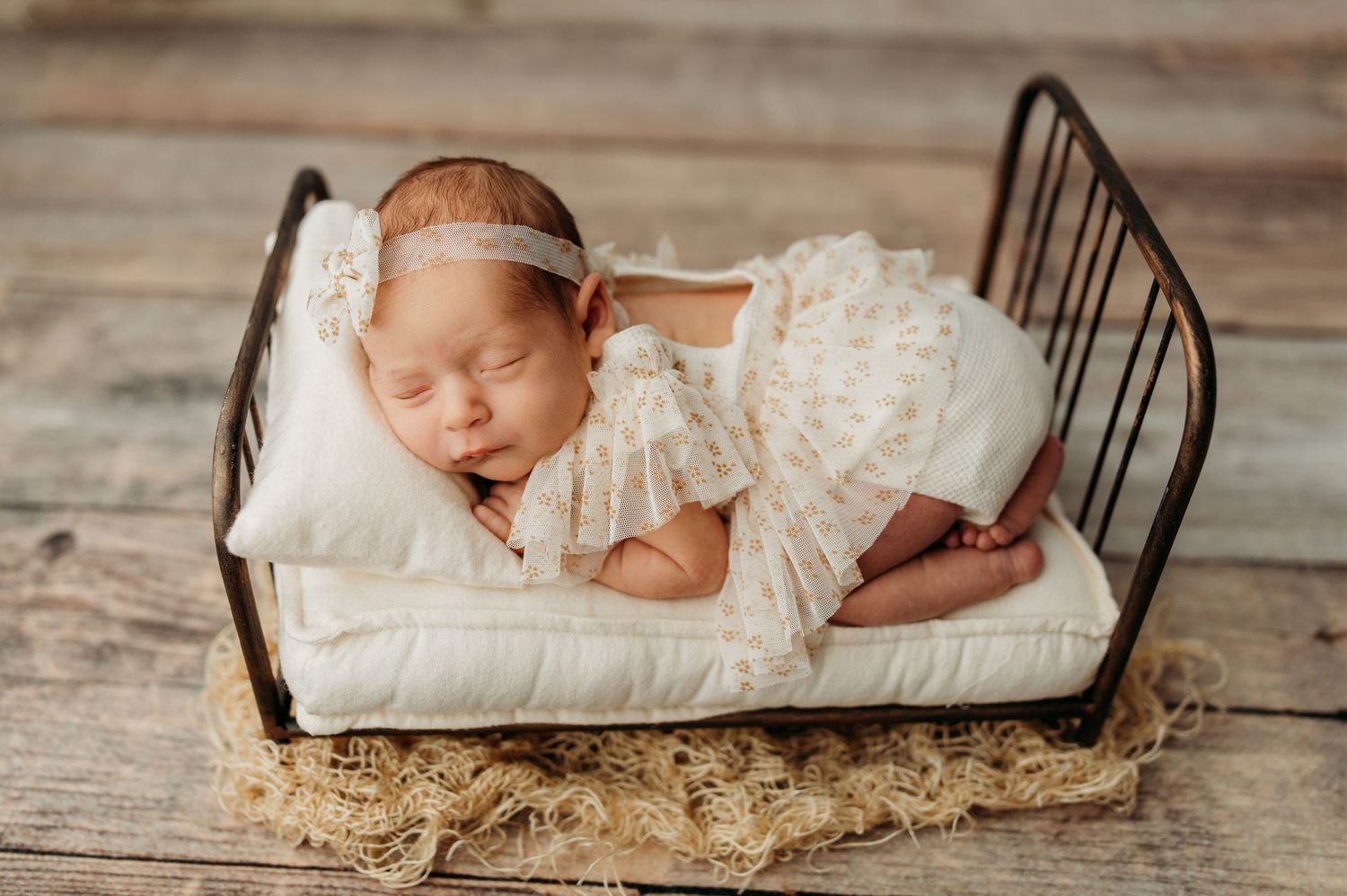 A sleeping newborn on white bedding with rustic wood textures in the background.