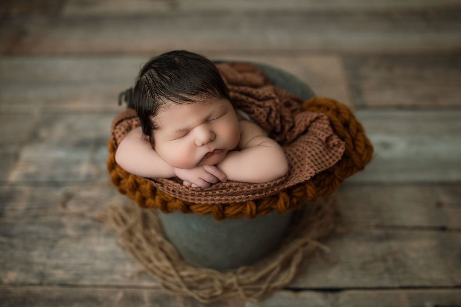 Newborn photography featuring rustic brown textures and vintage-style props on wooden flooring.