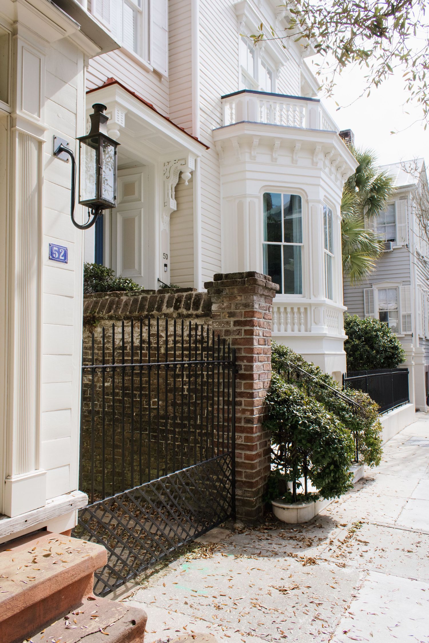 Classic white Charleston townhouse with bay window, brick fence and ornate iron gate on a tree-lined residential street.Charleston downtown