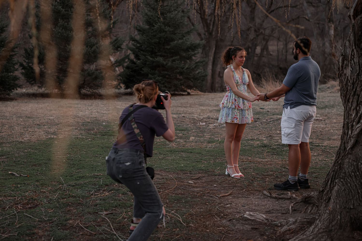 A photographer captures a couple posing together in a park during sunset.
