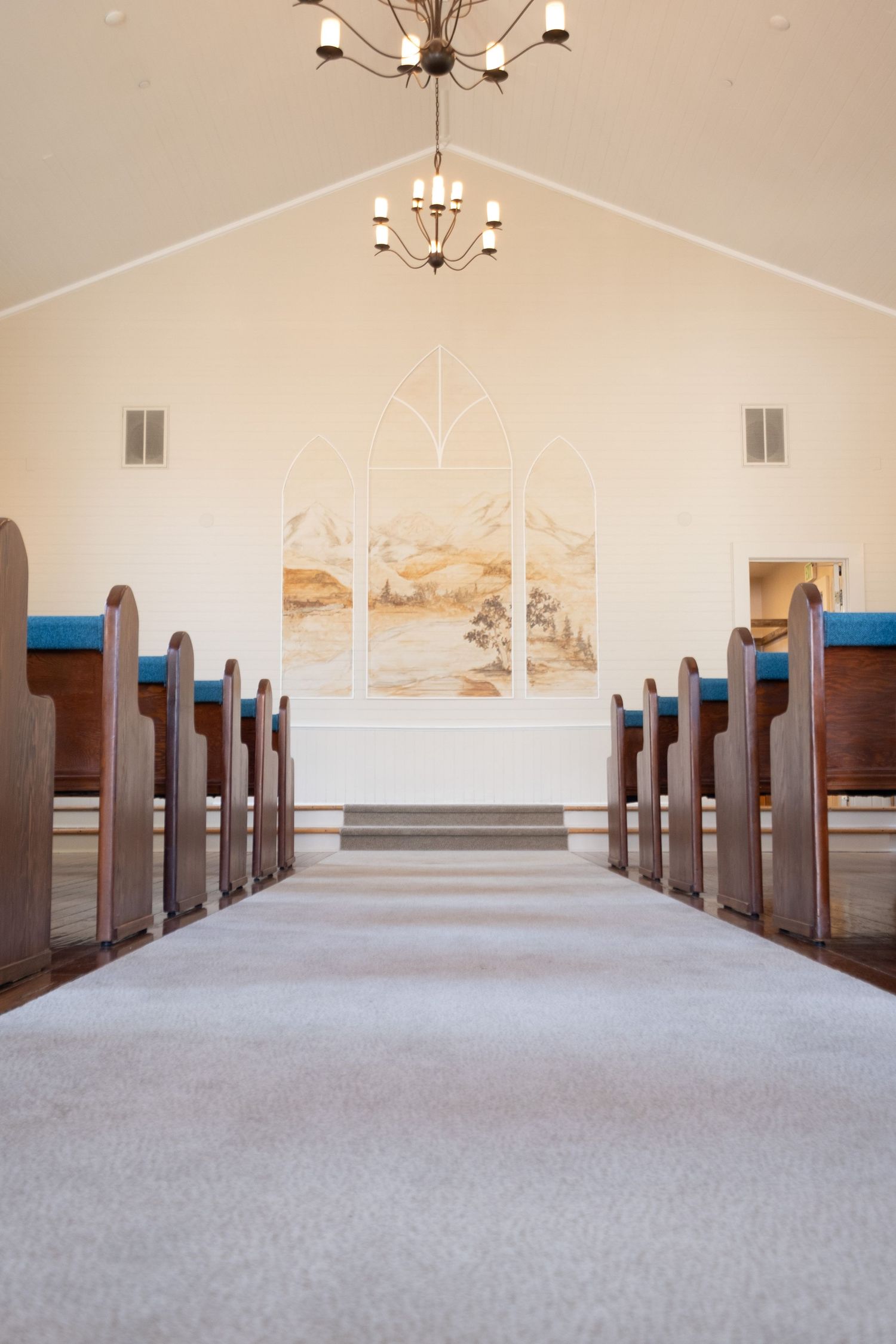 Interior of a modern church sanctuary with wooden pews and elegant chandeliers.