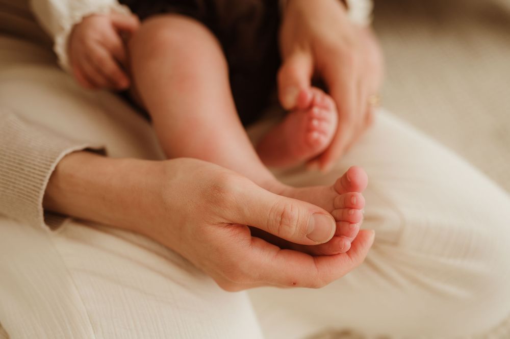 Gentle hands holding and massaging tiny baby feet on soft white fabric.