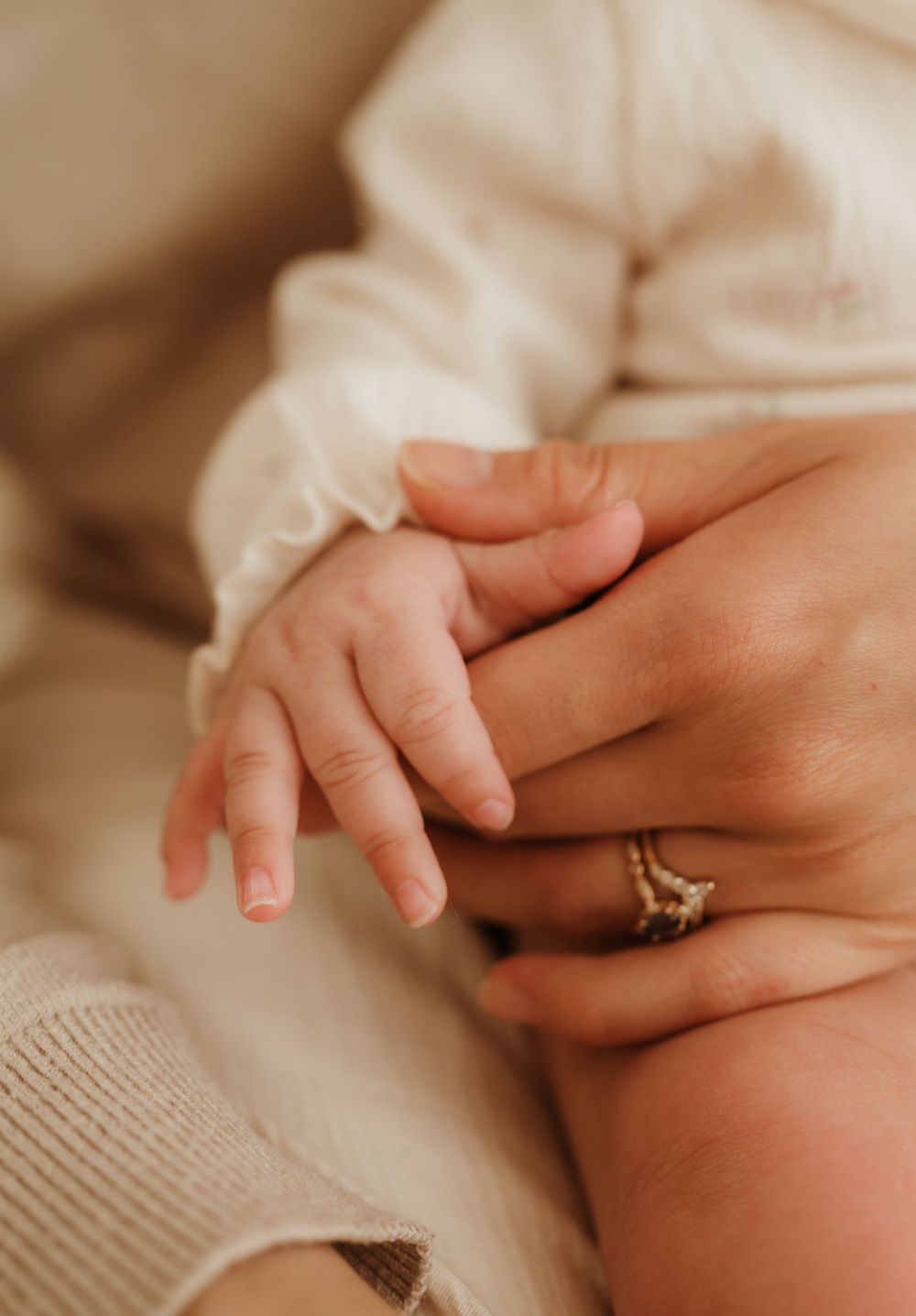 A close-up view of a small hand gently resting in another hand wearing a diamond engagement ring.