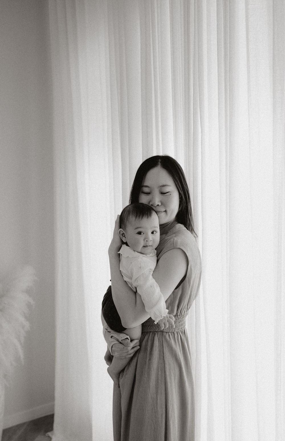 A series of black and white photos showing intimate moments between parent and child against a white curtain background.