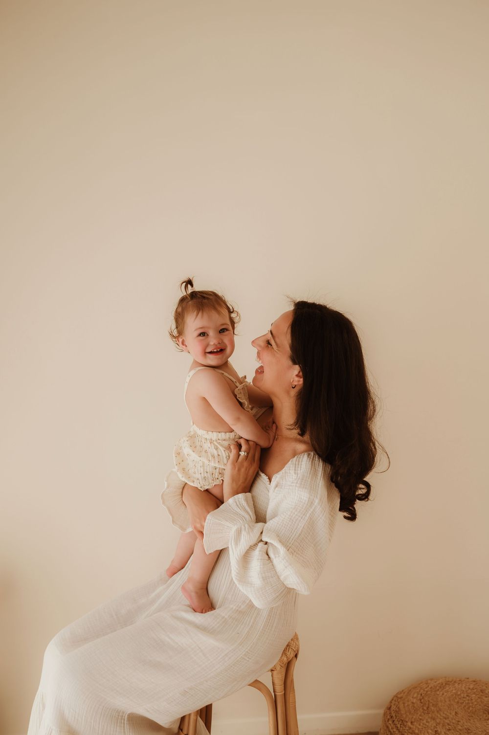 A joyful candid moment between parent and baby in matching white outfits against a neutral wall.