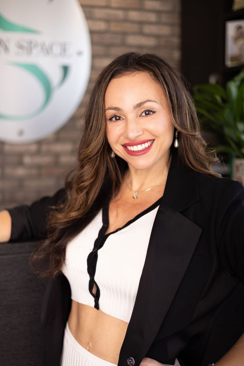 Woman in black blazer and white top smiling at Skin Space, brunette hair, professional beauty clinic portrait.