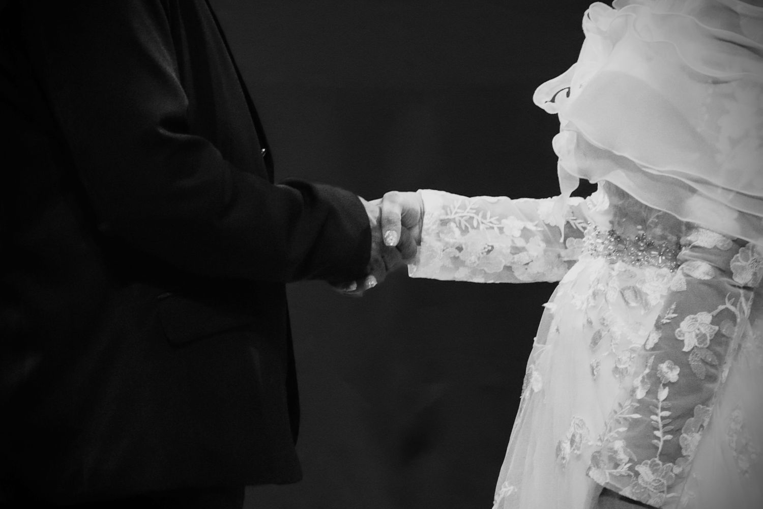 A close-up black and white photograph showing hands clasped together at a wedding ceremony.