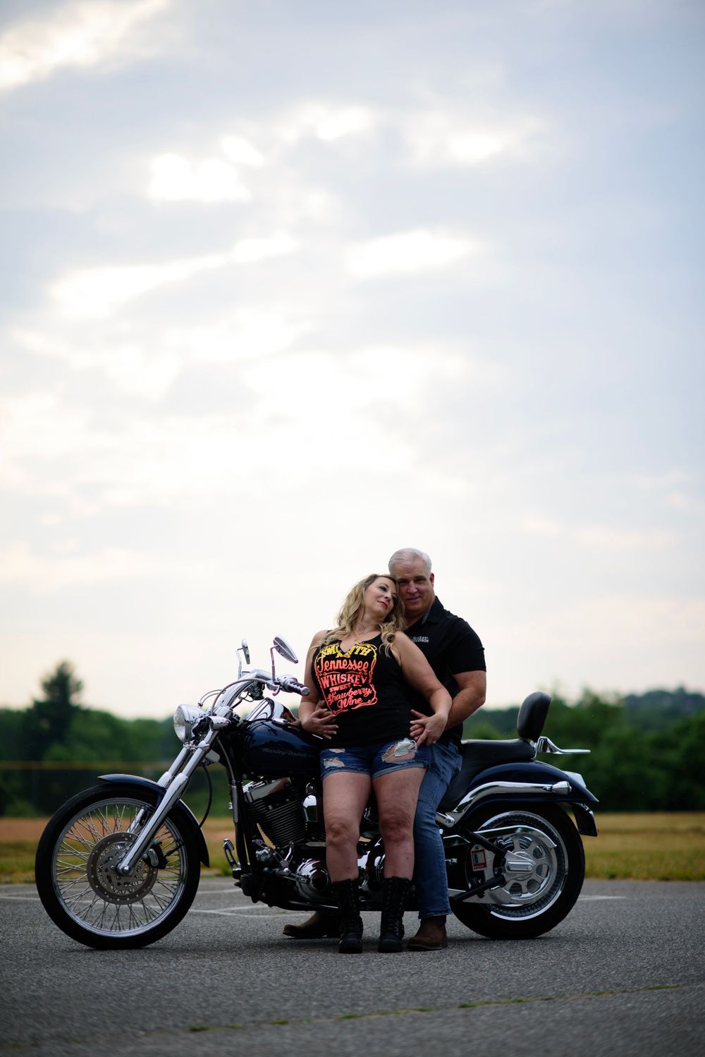 A couple shares an intimate moment while posing with their custom motorcycle on an empty road at dusk.