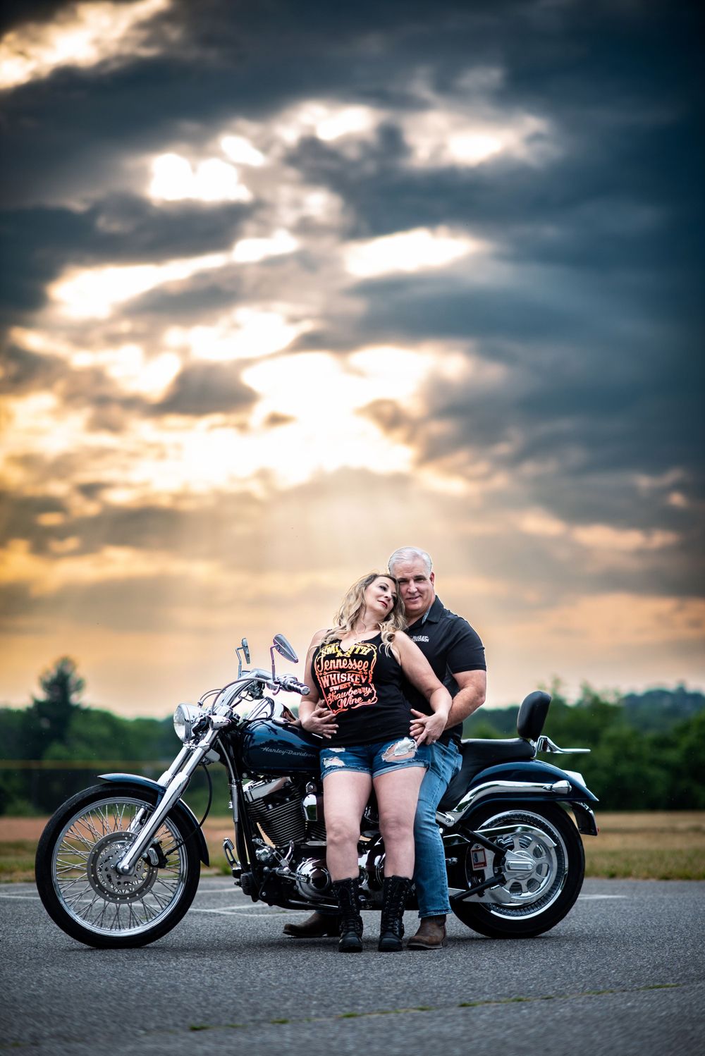 A motorcycle parked in front of a dramatic sunset sky with sunbeams breaking through dramatic clouds.