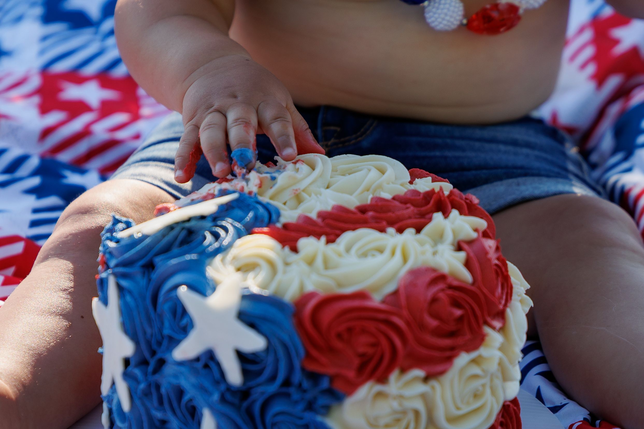 Baby touching a patriotic red, white, and blue rosette cake with star decorations for a first birthday smash cake celebration.