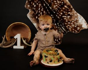 Baby's first birthday cake smash with deer hide, antlers, and number one sign on dark background.